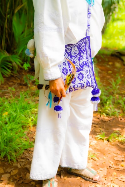A person in white traditional clothing holding a patterned blue bag and feathers
