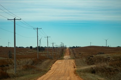 Dirt road leads through fields with power lines and windmills