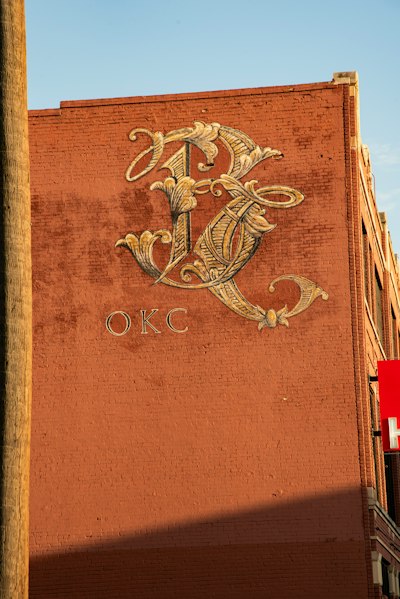 A large ornate monogram and the letters OKC painted on a red brick wall