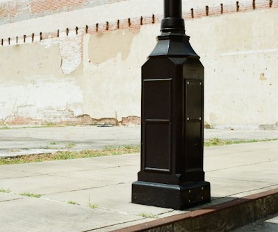 Black street lamp base on sidewalk against a textured wall