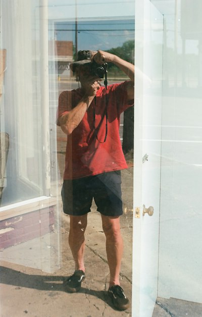 Man in red shirt reflecting in window holding camera