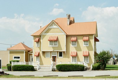 A yellow house with an orange roof and striped awnings