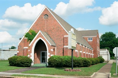 Red brick church building with an arched entrance and bushes