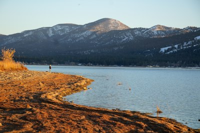a man standing on the shore of a lake with mountains in the background