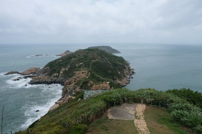 Green island peninsula jutting into the ocean under cloudy sky