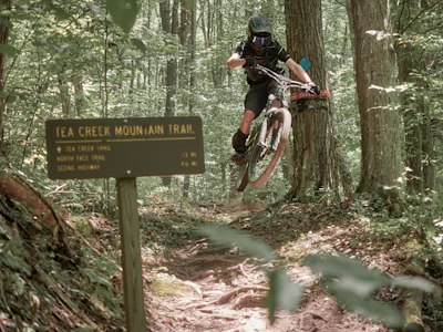Mountain biker jumps over a trail sign in a forest