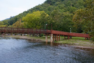 A brown pedestrian bridge spanning a river with a forested mountain in the background