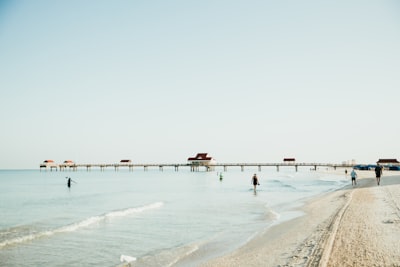 people are walking on the beach near a pier