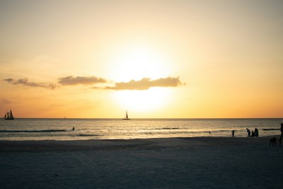 The sun is setting over the ocean with a sailboat in the distance