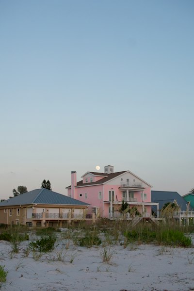 A pink house on the beach with a full moon in the sky
