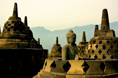 A stone Buddha statue among bell-shaped stupas at Borobudur temple in Indonesia