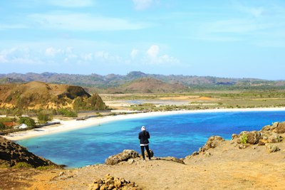 man in black jacket standing on brown rock near body of water during daytime