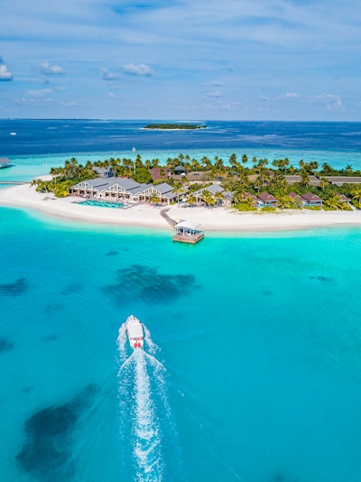 A boat traveling through turquoise water toward a tropical island resort in the Maldives