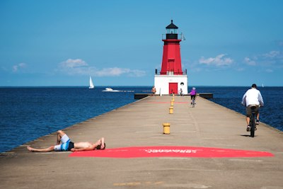 man in blue shorts lying on red concrete floor near white and red lighthouse during daytime