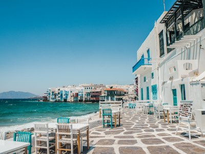 Tables and chairs on a stone patio beside the sea in Mykonos, Greece