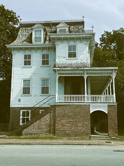 Weathered light blue victorian house with an ornate white porch