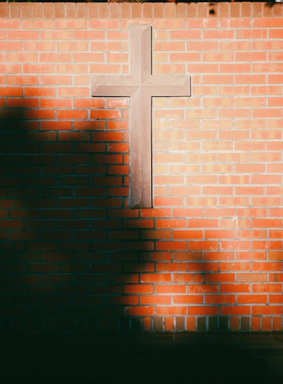 Stone cross on red brick wall with dappled shadows