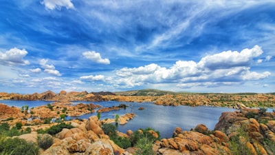 brown rocks on body of water under blue sky and white clouds during daytime