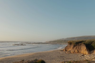 a sandy beach next to the ocean under a blue sky