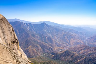 a man standing on top of a mountain next to a lush green hillside