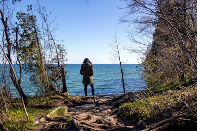 person in black jacket standing on brown log near body of water during daytime