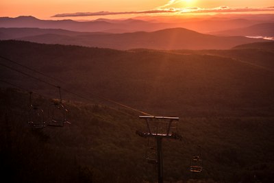 the sun is setting over the mountains and a ski lift