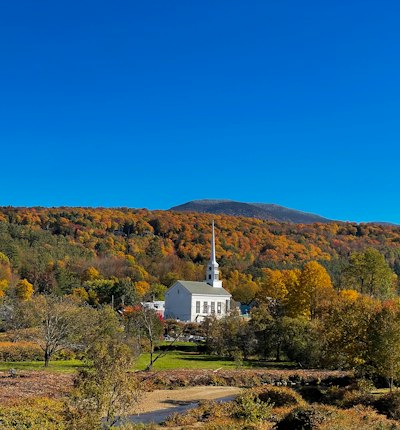 a church in the middle of a field with a mountain in the background